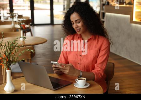 Frau, die ihr Smartphone benutzt, während sie im Café arbeitet Stockfoto