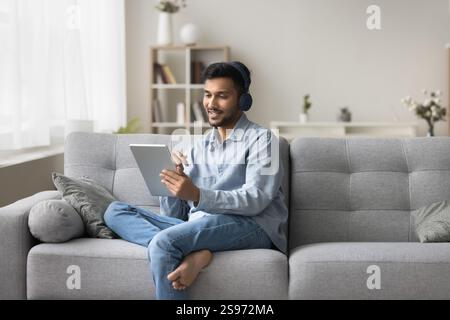 Lächelnder junger Mann im Headset auf dem Sofa sitzen Tablet verwenden Stockfoto