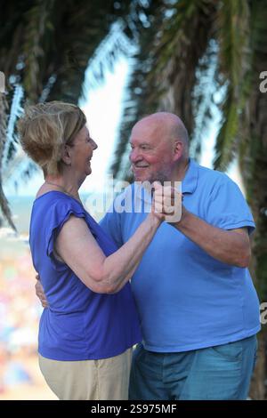 Älteres Paar tanzt und lächelt draußen am Sommertag mit Palmen im Hintergrund Stockfoto