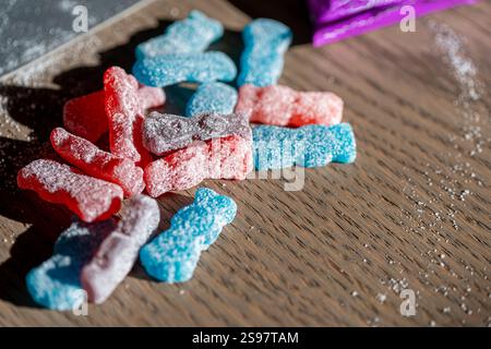 Eine bunte Auswahl an zuckerbeschichteten Gummibonbons in Rot-, Blau- und Violetttönen, die auf einer Holzoberfläche verstreut sind. Stockfoto