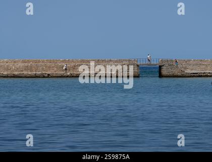 Chania - Kreta - 17. August 2024; Menschen auf einem Wellengang über den Hafen an einem wunderschönen mediterranen Tag. Stockfoto