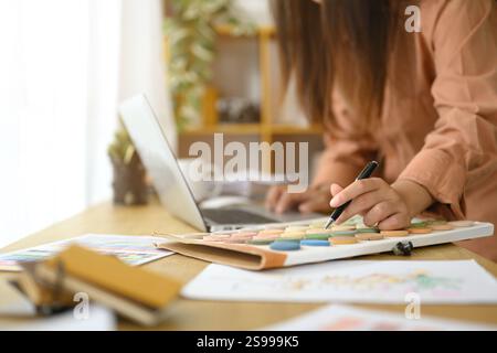 Innenarchitektin, die Farbmuster während der Arbeit an einem Laptop auswählt und überprüft Stockfoto