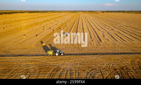 Bei zwei Traktoren, die beim Ziehen der Rundballenpresse das Stroh aufrollen und einen gepackten Rundballen über landwirtschaftlich gefallenen Ballenpressen ausspucken Stockfoto