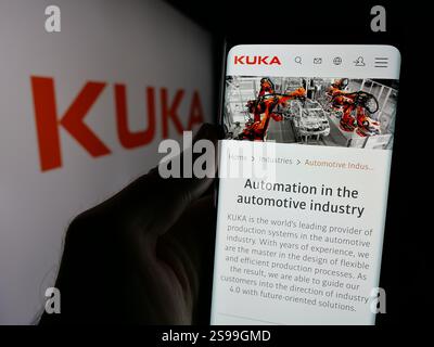 In dieser Fotoabbildung hält eine Person ein Handy mit der Webseite des deutschen Industrieautomationsunternehmens Kuka AG auf dem Bildschirm mit Logo. Stockfoto
