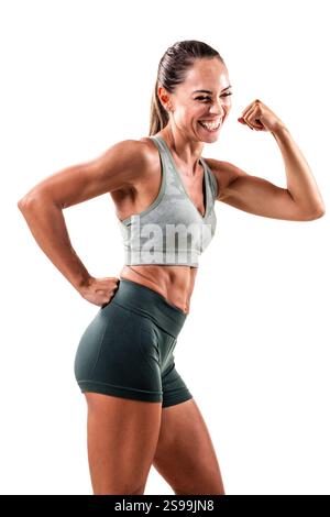 Eine fröhliche und fitte Frau posiert selbstbewusst, beugt ihre Arme, zeigt ihren fröhlichen Geist und ihr Engagement für Fitness, gekleidet in trendiger Sportkleidung Stockfoto