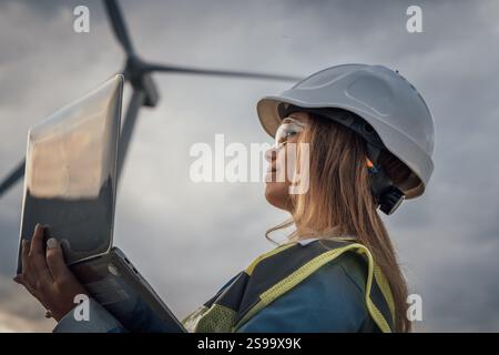 Eine erfahrene Ingenieurin nutzt ihren Laptop, um komplexe Windkraftanlagen zu überwachen, ihr Fachwissen unter Beweis zu stellen und Innovationen zu fördern Stockfoto