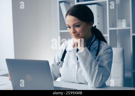 Eine engagierte und fokussierte Ärztin prüft mit ihrem Laptop wichtige Patientendaten gründlich und zeigt ihr Engagement für Stockfoto