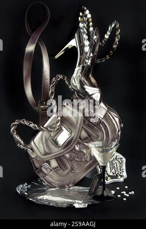 Ein metaphorisches Bild eines Metallic-Sets von Nachtclubaccessoires, das eine Geldbörse, weibliche Schuhe und Ornamente auf schwarzem Hintergrund enthält Stockfoto