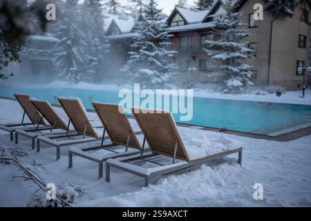 Warmer Freiluft-Swimmingpool mit blauem Wasser und schneebedeckten Liegestühlen bei kaltem Wetter, im Freien Stockfoto