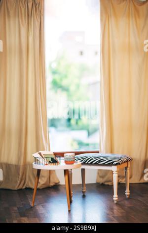 Stuhl mit gestreiftem Stoff und weißer Tisch vor Fensterhintergrund. Fotobereich mit Couchtisch Stockfoto