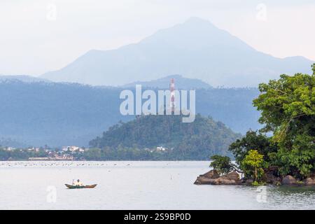 Malerischer Blick auf den Buhi-See in Bicol, Philippinen, mit einem Mann, der ein kleines Boot im Vordergrund paddelt, und üppige Berge im Hintergrund Stockfoto