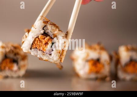 Essstäbchen nehmen eine Portion Sushi-Rolle. Sushi-Brötchen mit Lachsfrischkäse und Gurke. Isoliert. Sushi-Rolle auf grauem Hintergrund. Stockfoto