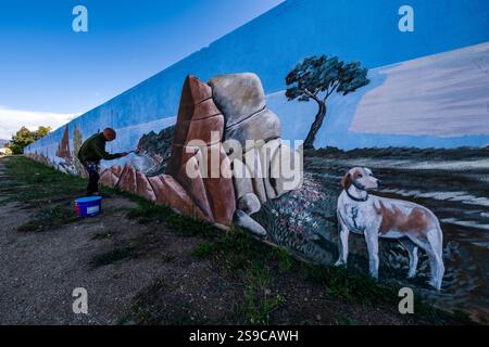 Ein Künstler malt ein farbenfrohes Graffiti mit einem Felsen und einem Hund an einer Wand. Stockfoto