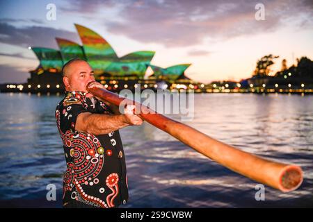 26. Januar 2025, Sydney, New South Wales, Australien: Man sieht, wie man während der Dawn Reflection vor dem beleuchteten Sydney Opera House ein Didgeridoo spielt. Der australische Nationaltag beginnt mit dem Dawn Reflection Event am 26. Januar 2025 in Sydney AustraliaÃ­s. Vor Sonnenaufgang wurden die Segel des Sydney Opera House mit dem Kunstwerk der Aborigines „River Life“ beleuchtet, das der Künstler James P. Simon geschaffen hat, um die Geschichte und Kultur der Aborigines zu feiern. (Credit Image: © George Chan/SOPA Images via ZUMA Press Wire) NUR REDAKTIONELLE VERWENDUNG! Nicht für kommerzielle USA Stockfoto