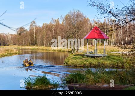 Zwei Männer in einer Bootsreihe einen Fluss hinunter, umgeben von lebhaftem Herbstlaub. Ein malerischer roter Pavillon steht am Ufer und verleiht der Ruhe Charme Stockfoto