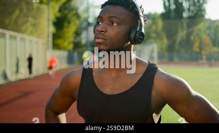 Nachdenklicher Afroamerikaner Sportler Sportler in Kopfhörern Smartwatch in der Stadt für Sporttraining vorbereiten männliche Läufer hören Musik in der Pause Stockfoto