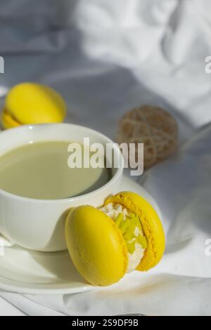 Süßes gelbes Macaron Dessert Tasse grüner Matcha Tee Latte auf Pflanzenbasis in gemütlicher Morgenliegenatmosphäre. Kreative Urlaubsidee mit romantischem Date. Pflanzliche präbiotische Faser Superfood Getränk Antioxidans-reiche Immunität-Boosting Kaffee Alternativen Getränk Stockfoto