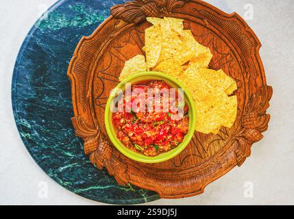 Flacher Blick über dem Kopf auf frische hausgemachte Salsa aus Bio-Tomaten und Basilikum in einer Vintage-Schüssel und Bio-Maischips auf einem antiken Holztablett Stockfoto
