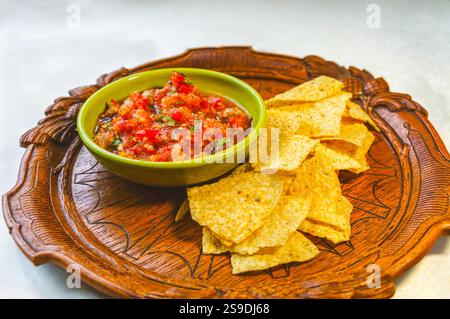 Frische hausgemachte Salsa aus Bio-Tomaten und Basilikum in einer Vintage-Schüssel und Bio-Maischips auf einem antiken Holztablett. Stockfoto