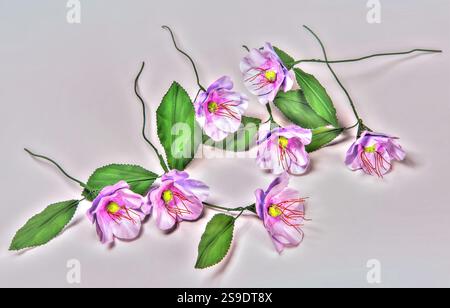 Elegante Ausstellung künstlicher violetter Blumen mit leuchtend roten Staubblättern und hellgrünen Blättern, wunderschön auf einer glatten Oberfläche angeordnet. Highlights Stockfoto