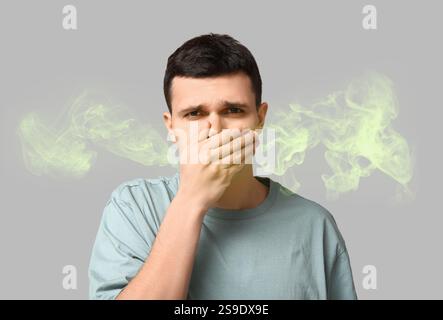 Junger Mann, der einen schlechten Geruch aus seinem Mund auf grauem Hintergrund spürt Stockfoto