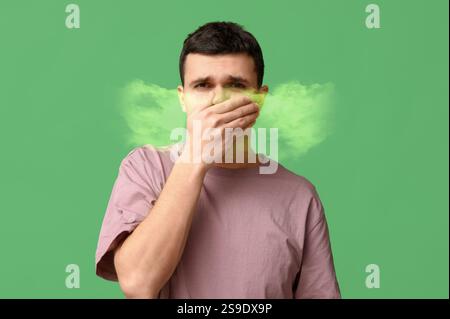 Junger Mann, der einen schlechten Geruch aus seinem Mund auf grünem Hintergrund spürt Stockfoto