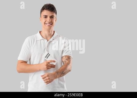 Junger Mann, der Creme auf seinem tätowierten Arm vor hellem Hintergrund aufträgt Stockfoto