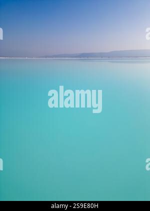 Ein faszinierender türkisfarbener See mit sanftem Himmel und einem ruhigen Horizont. Das ruhige Wasser und die minimalistische Komposition betonen die Harmonie und Stockfoto