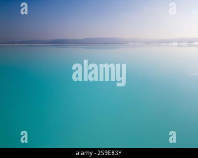 Ein faszinierender türkisfarbener See mit sanftem Himmel und einem ruhigen Horizont. Das ruhige Wasser und die minimalistische Komposition betonen die Harmonie und Stockfoto