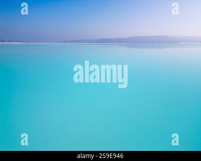 Ein faszinierender türkisfarbener See mit sanftem Himmel und einem ruhigen Horizont. Das ruhige Wasser und die minimalistische Komposition betonen die Harmonie und Stockfoto