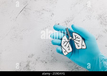 Die Hände des Arztes tragen Handschuhe und halten Lungen-Papier für den Welt-TB-Tag. Förderung des Bewusstseins für Lungengesundheit, Tuberkuloseprävention und Atemwegspflege Stockfoto