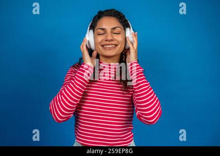 Glückliche junge Frau, die Musik mit kabellosen Kopfhörern hört, den Klang genießt und mit geschlossenen Augen lächelt Stockfoto