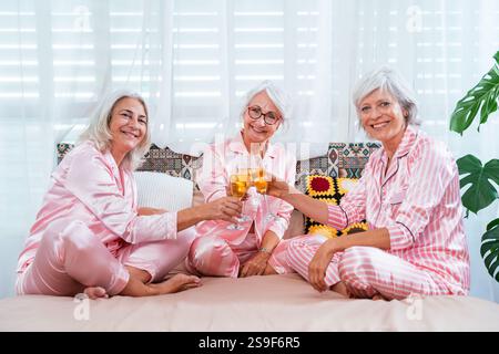 Schöne ältere Frauen, die zu Hause eine lustige Pyjama-Party feiern - Gruppe von fröhlichen älteren Freundinnen, die Spaß haben und mit Wein feiern, Konzepte abo Stockfoto