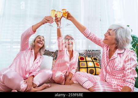 Schöne ältere Frauen, die zu Hause eine lustige Pyjama-Party feiern - Gruppe von fröhlichen älteren Freundinnen, die Spaß haben und mit Wein feiern, Konzepte abo Stockfoto