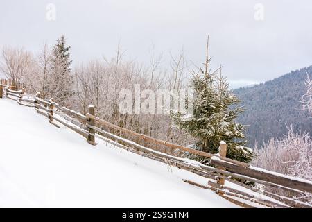 Ländliche Landschaft im Winter. Weiße Saison. Holzzaun durch schneebedeckten Hügel Natur Hintergrund Stockfoto