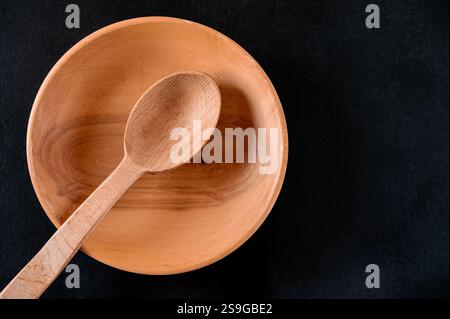 Brauner Holzlöffel in Holzteller auf schwarzem Tisch Stockfoto