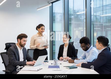 Erfolgreiches, vielseitiges Geschäftsteam, Gruppe von Geschäftsfrauen und Geschäftsmännern, die sich unterhalten und zusammenarbeiten, zufriedene und lächelnde Mitarbeiter im Büro, am Konferenztisch. Stockfoto