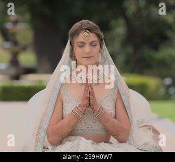 Atemberaubende kaukasische Braut in indischem Brautkleid im Gebet mit gefalteten Händen für ihre hinduistische Hochzeitszeremonie Stockfoto