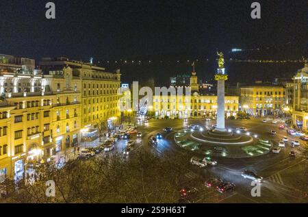 Blick auf die Drohne auf den Freiheitsplatz (Turm) und die Statue in der Ferne in elektrtischen Lichtern der Stadtbeleuchtung in Tiflis. Kreisverkehr dort. Glas r Stockfoto