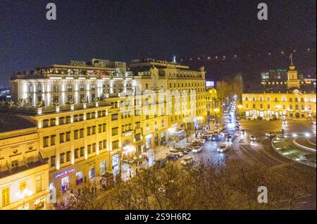 Drohnenblick auf einen Teil des Freiheitsplatzes (Turm) und Statue in der Ferne in elektrtischen Lichtern der Stadtbeleuchtung in Tiflis. Kreisverkehr dort. Stockfoto