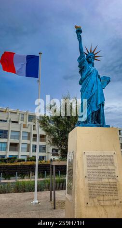 Die Freiheitsstatue, die Freiheit, die die Welt erleuchtet, in der Nähe der französischen Flagge, die im Wind fliegt. 30. Juni 2023. Soulac-sur-Mer, Nouvelle-Aquitaine Stockfoto