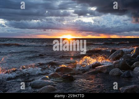 Heller Sonnenuntergang über der Ostsee in Estland: Wellen krachen gegen das felsige Ufer und färben den Sprühnebel in goldenen Tönen. Stockfoto