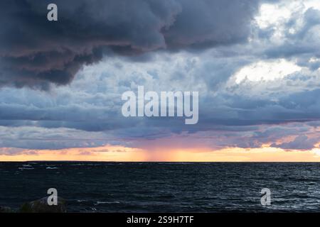 Dramatische Sturmwolken sammeln sich über der turbulenten Ostsee, die bei einem windigen Sonnenuntergang von einem Lichtstrahl beleuchtet werden. Stockfoto