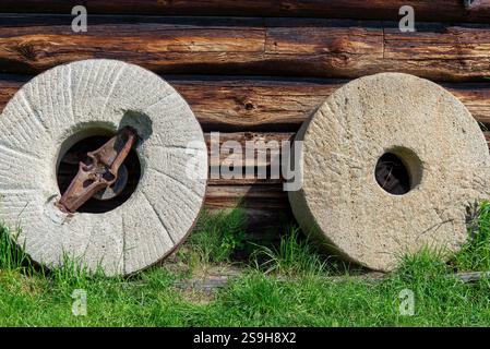 Mühlsteine, die an die Wand eines alten Holzhauses gelehnt sind. Stockfoto