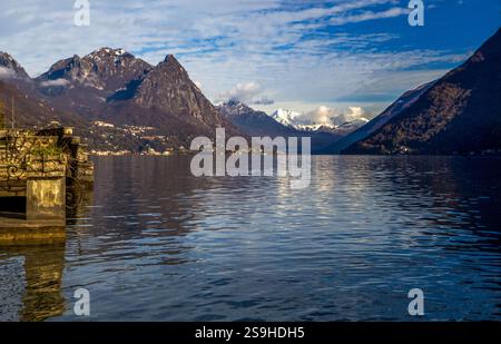 Atemberaubende schneebedeckte Berge am Lugani-See im Winter - Schweizer Alpen oder europäische Alpen im Vorort Lugano. Im vorderen Teil des Piers (vielleicht kleines Hotel) Stockfoto