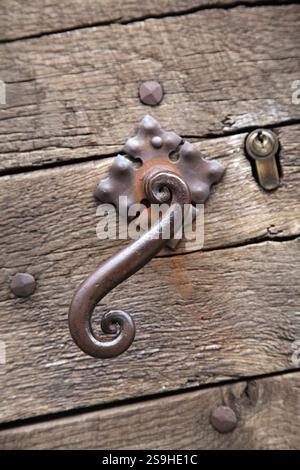 Nahaufnahme einer kunstvollen Metallverriegelung an einer rustikalen Holztür in Sarlat-la-Caneda, die lokale Handwerkskunst hervorhebt. Stockfoto