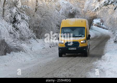 Ein gelber DHL-Lieferwagen, der auf einer schneebedeckten Landstraße fährt, gesäumt von schneebedeckten Bäumen Stockfoto