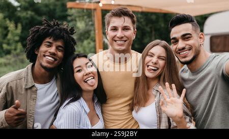 Glückliche, vielfältige junge Freunde posieren in der Nähe von Wohnmobil, Spaß haben, albern sein, zeigen verschiedene Gesten auf Campingausflug Stockfoto