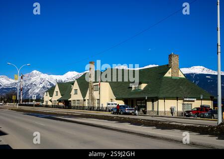 Ein großes Gebäude mit einem grünen Dach befindet sich an einer Straße mit klarem blauem Himmel. Das Gebäude ist von Autos und ein paar Leuten umgeben Stockfoto