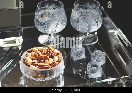 Mischen Sie Nüsse in einer Glasschale auf einem Serviertablett mit zwei leeren Gläsern, Eiswürfeln und einer Flasche Stockfoto